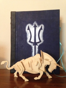 a wooden model approximating a bull skeleton standing before a large, blue-bound book emblazoned with a trident